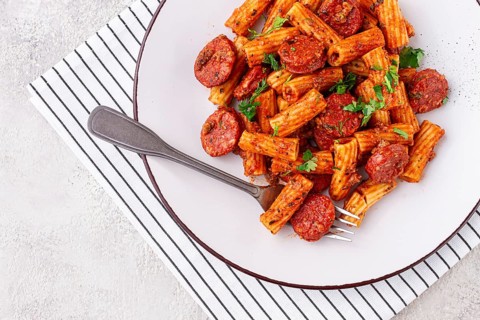 Rigatoni pasta with spicy sausage, and rich tomato sauce served, on a white plate, homemade