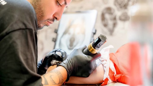 A skilled tattoo artist intently focuses on creating an intricate ink design on a client's arm,
