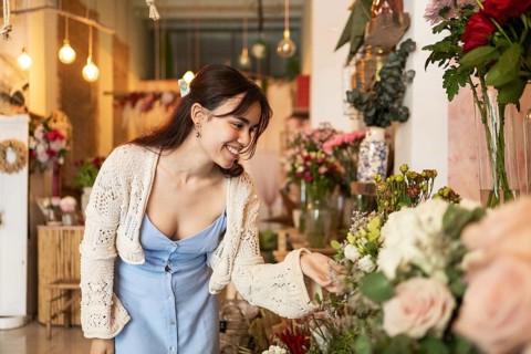 A smiling woman admires a variety of colorful flowers in a cozy flower shop. The warm lighting and