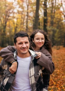 A joyful father and daughter embrace in an autumn forest. The vibrant fall foliage creates a warm