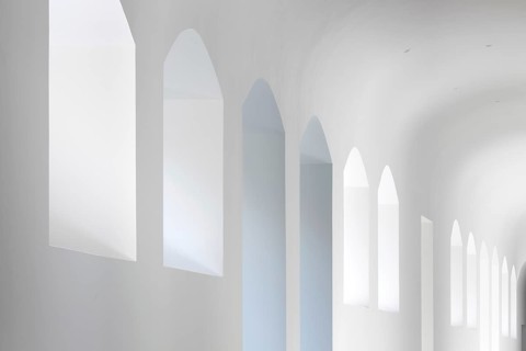 A serene view of arched windows in a minimalist white interior of a hospital. The soft lighting and