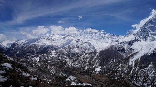 Wide valley of towering, snow-capped mountains in the Himalayas with dramatic skies, trekking at