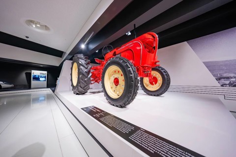 Side perspective of a red tractor in a modern exhibition hall, Porsche Museum, Stuttgart, Germany
