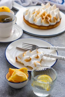 A slice of homemade lemon cake with golden peaks served on a plate, accompanied by a cup of tea,
