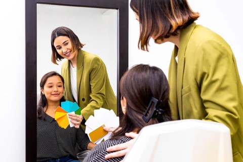 A professional image consultant advises a woman in front of a mirror, showing various color swatch
