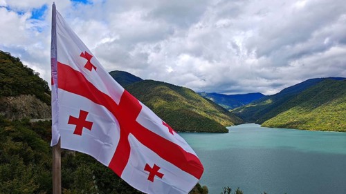 Georgian flag waving against a landscape of lakes and mountains, Georgia