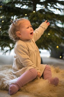 Toddler sits whining on a carpet in front of a decorated Christmas tree