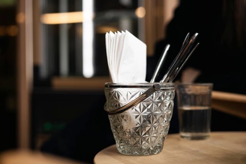 A detailed close-up of a glass container holding napkins and straws on a cafe table, paired with a
