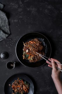 Top view of crop unrecognizable person taking food with chopsticks from plate with Korean dish