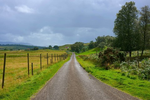 Long country road between green fields and trees, cloudy sky, Sutherland, Strathnaver, Kinbrace,