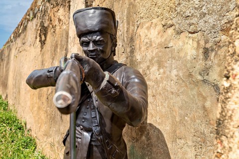Bronze statue of an aimless soldier with a rifle in front of a wall, statue in the historic