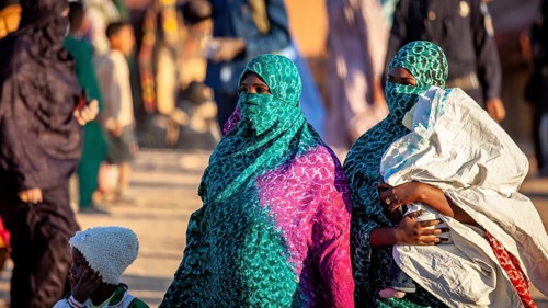 Two woman in green and blue robes march on a street, Veiled woman at the Tamanrasett Festival in