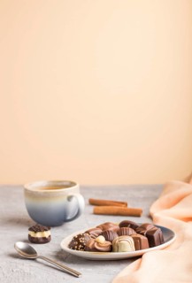 Different chocolate candies and a cup of coffee on a gray and orange background and orange textile.