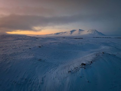 A tranquil winter scene captures Iceland's snow-blanketed land under a vast sky at dusk. Subtle