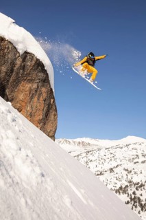 A snowboarder in bright gear descends a steep, snow-covered mountain slope, expertly navigating