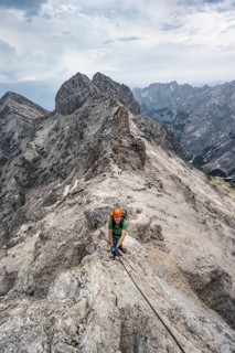 Mountaineer with helmet climbing in a secured climb on the rock, on a narrow rocky ridge, crossing