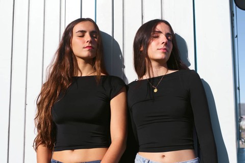Two women friends bask in the warm sunlight, their expressions relaxed and serene. Standing against