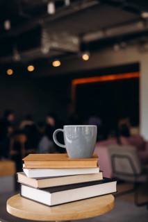 A serene coffee shop scene featuring a stack of books and a mug on a round table. The warm lighting