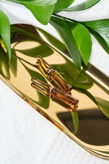 Three glass cosmetic ampoules containing concentrated anti-aging serum, arranged on a reflective