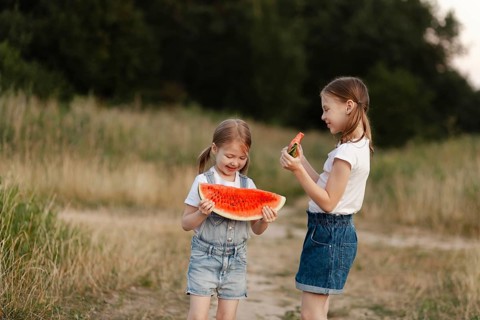 Two young children delight in juicy watermelon slices outdoors during a sunny summer day. Their