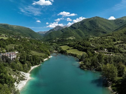 Aerial view of Lago di Fiastra in Italy, featuring turquoise waters, lush green hills, and clear