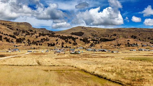 Rural scene with scattered houses in front of mountains under a dramatic sky, The villages and