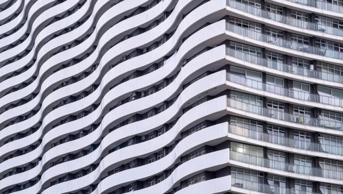 The wavy facade of a modern high-rise building in an urban environment. The repetitive pattern of