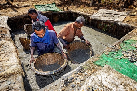 Group of men work together to filter raw materials from a pool of water with baskets, the sapphire