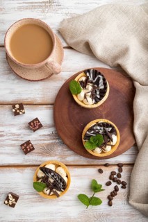Sweet tartlets with chocolate and cheese cream with cup of coffee on a white wooden background and
