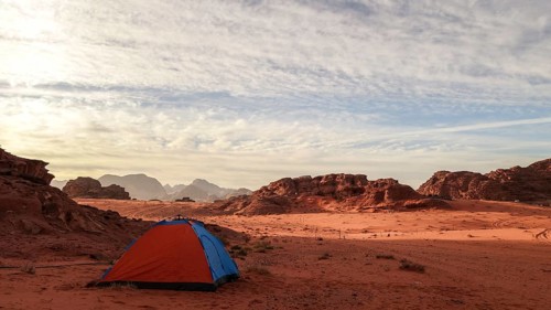 A vibrant orange tent pitched against the dramatic background of Wadi Rum's rocky mountains under a