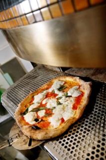 A freshly baked pizza topped with tomatoes, basil, and mozzarella cheese is being removed from an