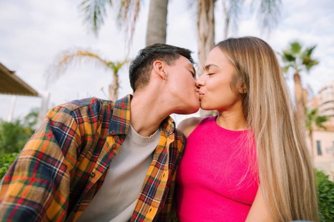 A joyful lesbian couple shares a loving kiss outdoors, surrounded by lush greenery. Their happiness