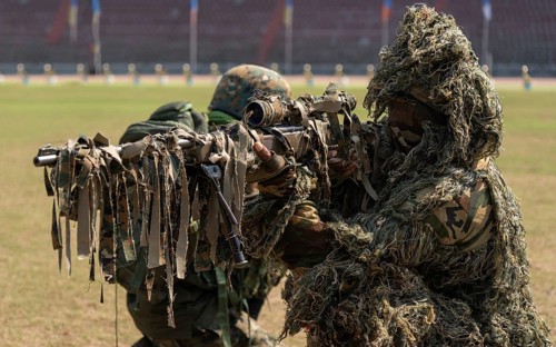 A camouflaged sniper of the Central Reserve Police Force takes aim during a tactical demonstration