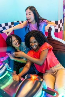 Group of young women having fun together playing an arcade racing game at an entertainment venue