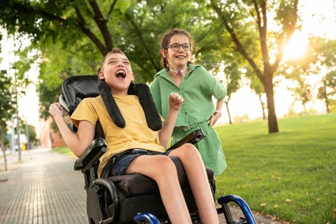 A boy with cerebral palsy in a wheelchair and a girl with a tracheostomy share a joyful moment in a