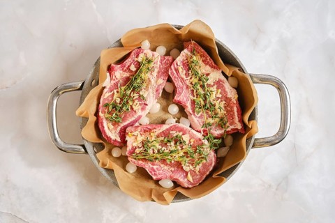 Pork rib chops are placed in a cooking pan lined with parchment paper. The meat is seasoned and