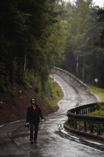 A lone traveler explores a wet, winding road through Norway's lush forest, embodying the spirit of