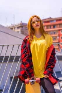 Skateboarder woman with a yellow t-shirt, red plaid shirt and sunglasses, in a pose with