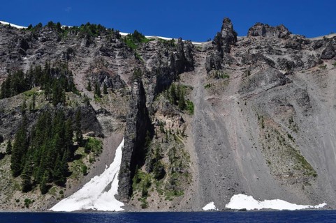Steep rock walls, called the devil's backbone, with trees and snow over a lake, Crater Lake