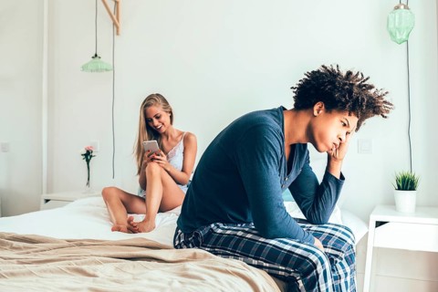 A couple in a modern bedroom. One person looks distracted with a phone while the other appears