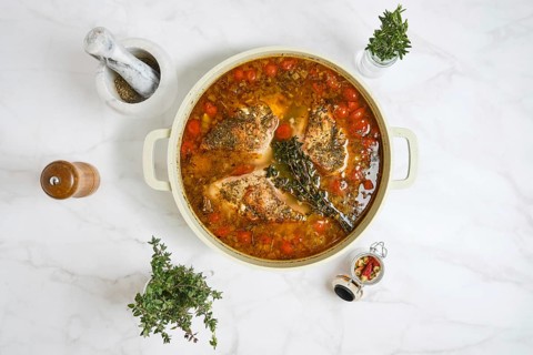 Rabbit meat is simmering in a pot with vegetables and herbs. The dish is prepared on a marble