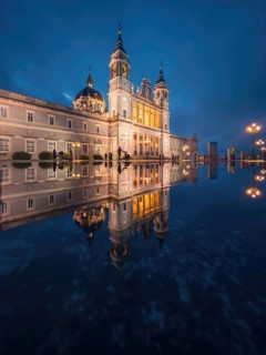 The majestic Almudena Cathedral of Madrid illuminated at dusk, its ornate architecture mirrored