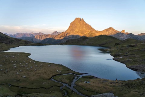 Captivating view of the Midi d'Ossau summit reflected in a peaceful lake, surrounded by lush
