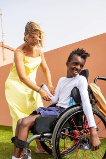 A woman in a yellow dress helps a cheerful boy in a wheelchair with cerebral palsy in pool. Their