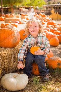 Little Boy Sitting and Holding His Pumpkin in a Rustic Ranch Setting at the Pumpkin Patch