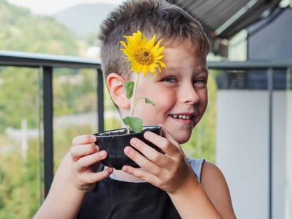 A smiling young boy holding a small sunflower in a pot, representing growth and care, with a serene