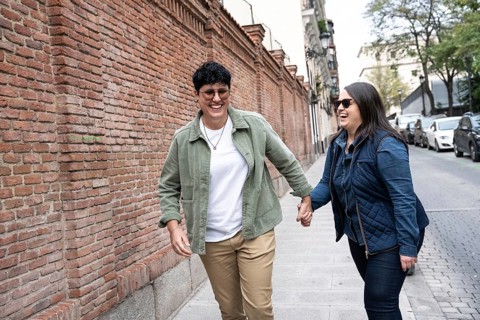 A joyful curvy lesbian couple strolling hand in hand along an urban street. They are laughing and
