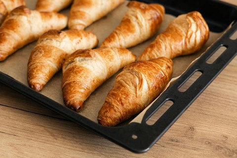 Golden homemade croissants sit fresh from the oven on a baking tray. The flaky, buttery pastry