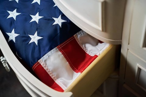 A neatly folded American flag rests inside a wooden drawer, displaying its stars and stripes. This