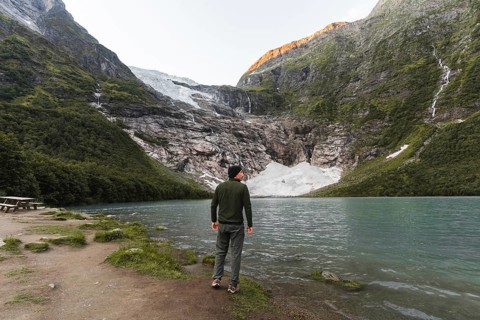 A man stands by a turquoise lake, gazing at a glacier nestled in Norway's mountains The golden